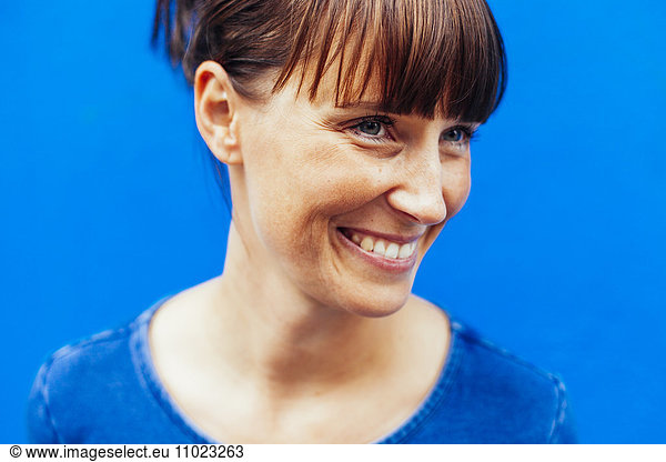 Close-up of happy woman looking away against blue background