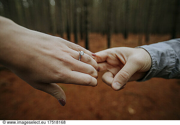 Close up of holding hands in woods with engagement ring.