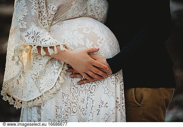 Close up of husband and pregnant wife hands touching belly outdoor