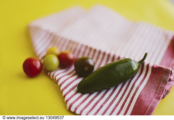 Close-up of jalapeno pepper and cherry tomatoes on textile over yellow background