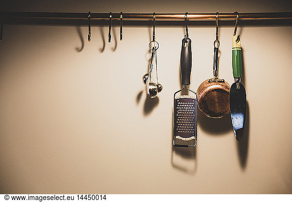 Close up of kitchen utensils suspended from copper pipe.