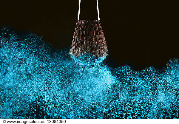 Close-up of make-up brush with blue face powder against black background