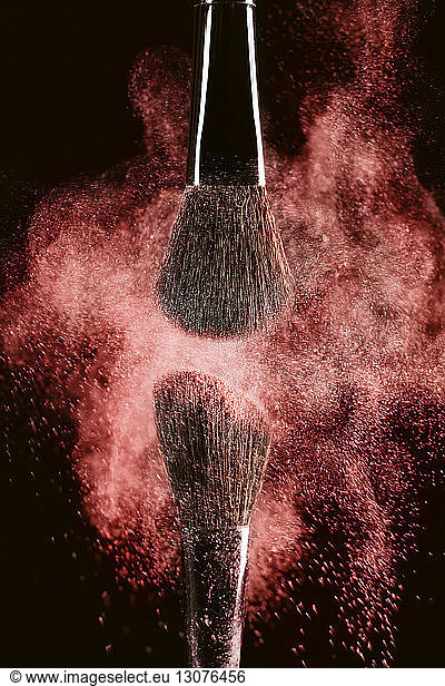 Close-up of make-up brushes with red face powder against black background