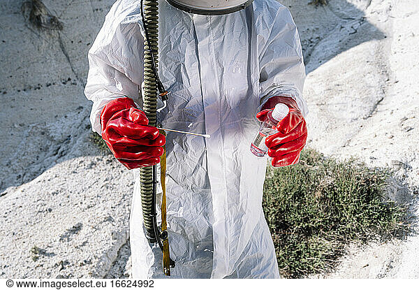 Close-up of male astronaut holding bottle and cotton swab while standing on snow covered land