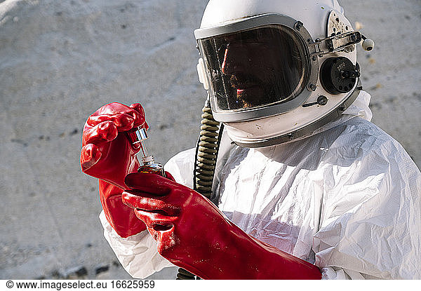 Close-up of male astronaut holding bottle while doing research on planet