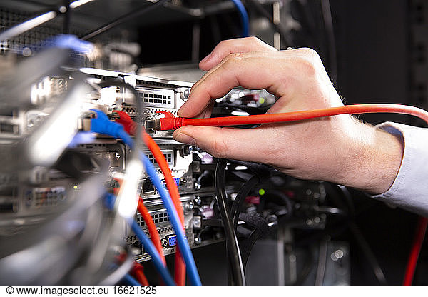 Close-up of male engineer examining network connection plug in data center