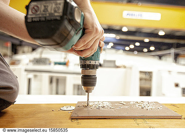 Close up of man drilling wood with a drill machine in a workshop
