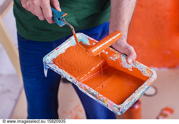 Close-up of man holding paint tray with orange paint
