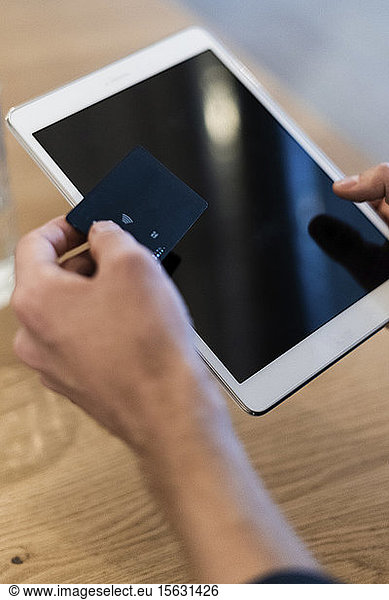 Close-up of man using tablet and holding credit card