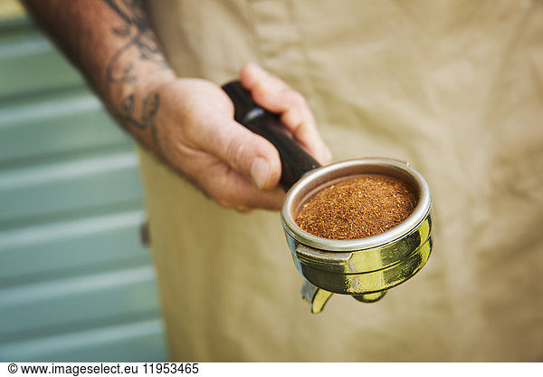 Close up of man with tattoo on his arm holding portafilter for espresso machine.