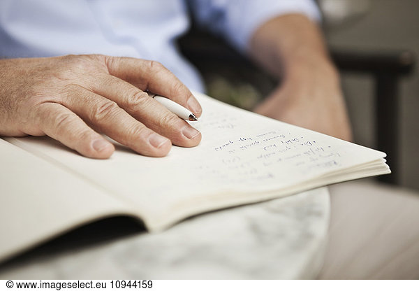 Close up of mature man's hand holding pen with book