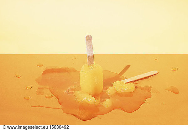 Close-up of melting popsicles on table against yellow background