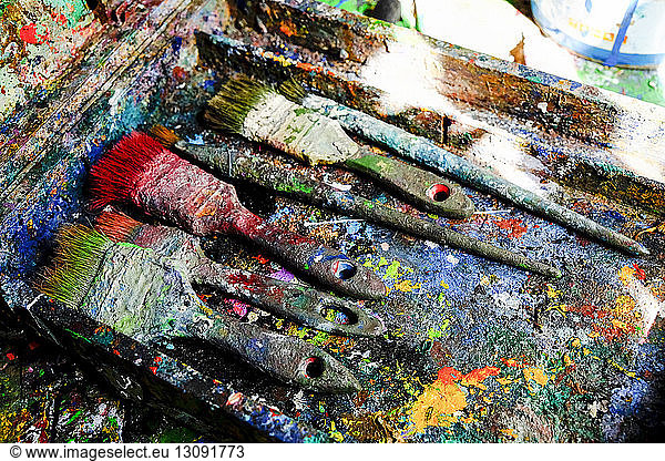 Close-up of messy paintbrushes in dirty colorful stained container on table