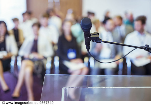 Close-up of microphone and transparent lectern with audience seen in blurred background