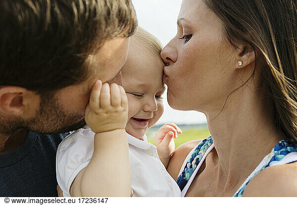 Close up of mid adult parents kissing baby daughter