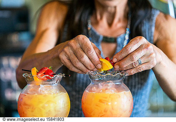 Close up of middle aged woman's hands making drinks with fruit