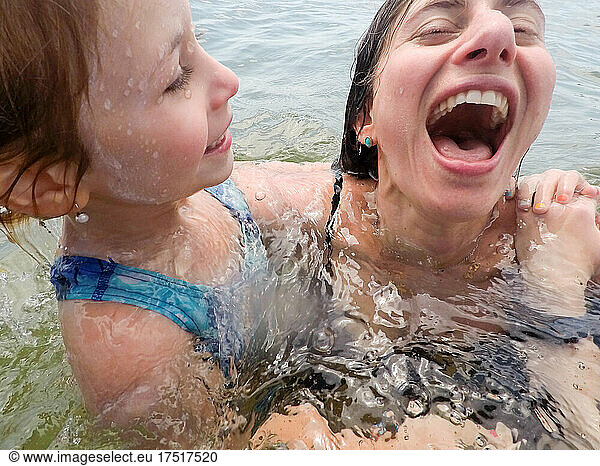 close up of mother and daughter laughing while in ocean together