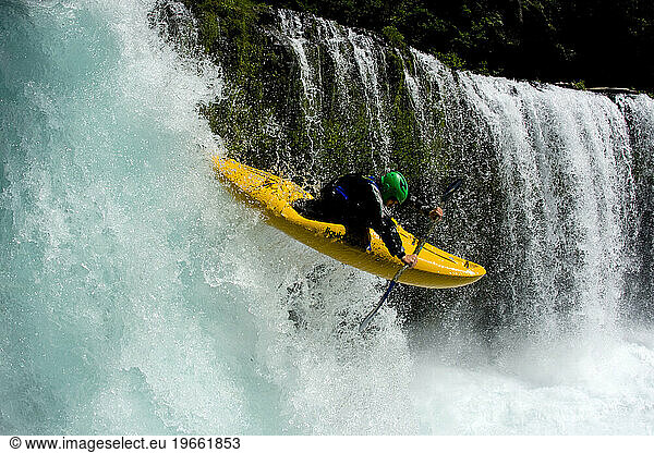 Close up of one male kayaker halfway down a waterfall in clear blue water.