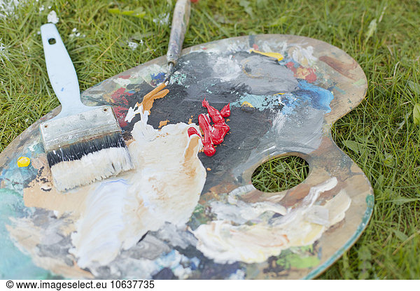 Close-up of paintbrush and painting knife on messy palette in backyard