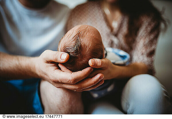 Close up of parents' hands holding baby newborn head full of hair