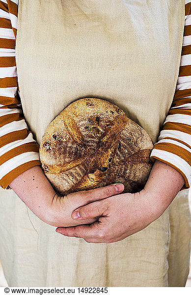 Close up of person holding a freshly baked round loaf of bread.
