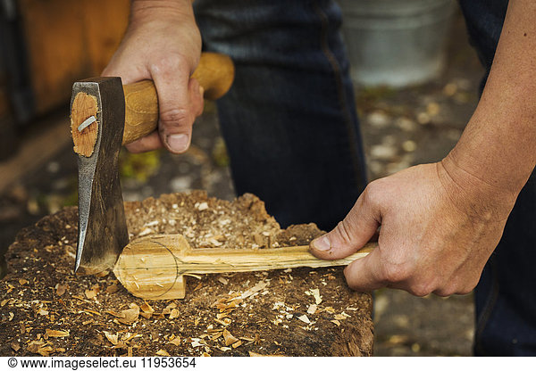 Close up of person holding a hand axe  cutting and shaping a small piece of wood on a splitting block covered in wood shavings.