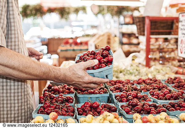 Close up of person holding punnet with fresh red cherries at a fruit and vegetable market.