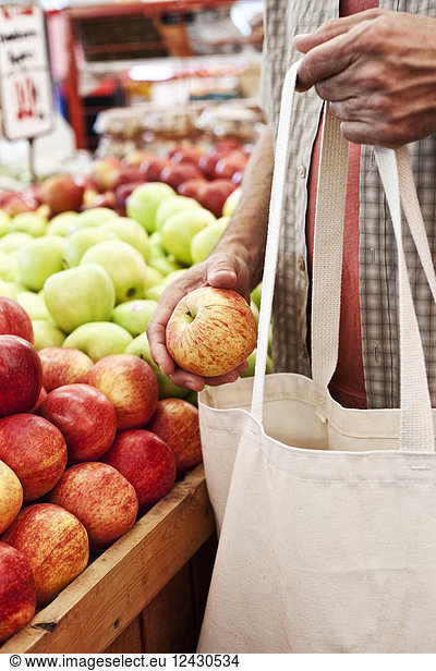 Close up of person holding shopping bag and red apple at a fruit and vegetable market.