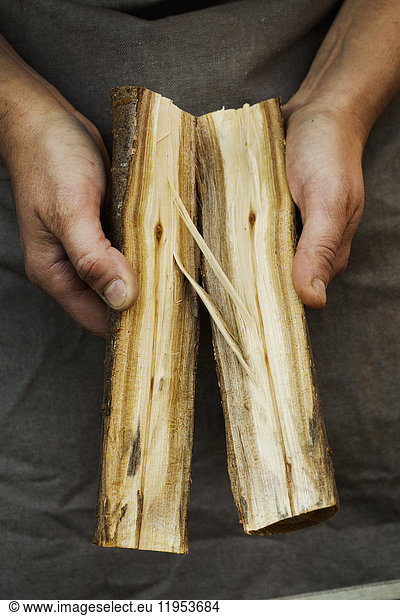 Close up of person holding two pieces of a log of wood split in half. Wood grain knots and pattern.