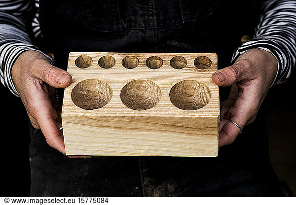 Close up of person holding wooden block with circular holes in different sizes.