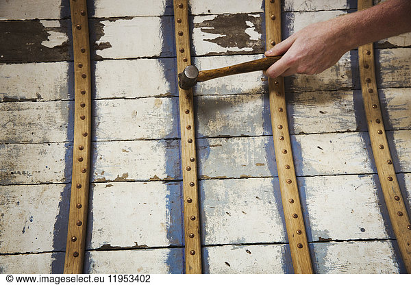 Close up of person in a boat-builder's workshop  working on a wooden boat hull.