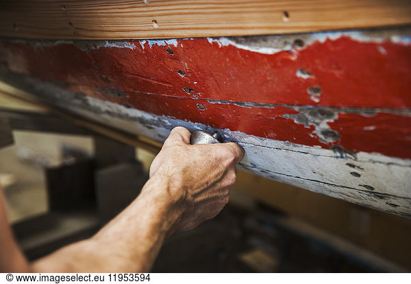 Close up of person in a boat-builder's workshop  working on a wooden boat hull.