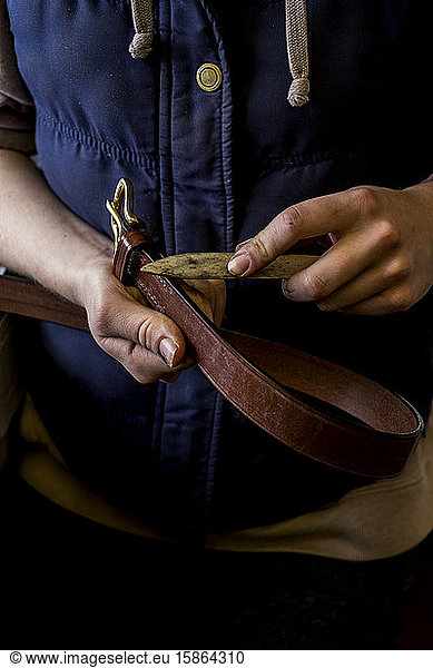 Close up of person in saddler's workshop holding leather strap.