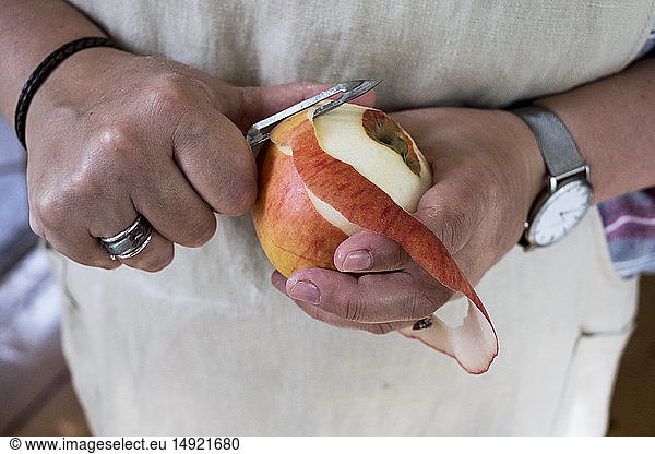 Close up of person peeling a red apple with a double bladed peeler.