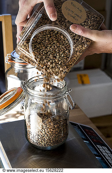 Close up of person pouring brown lentils into glass jar on kitchen scales.