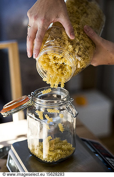 Close up of person pouring Fusilli pasta into glass jar on kitchen scales.