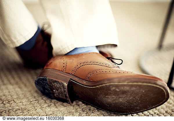 Close up of person's feet  wearing brown leather brogues  blue socks and white trousers.