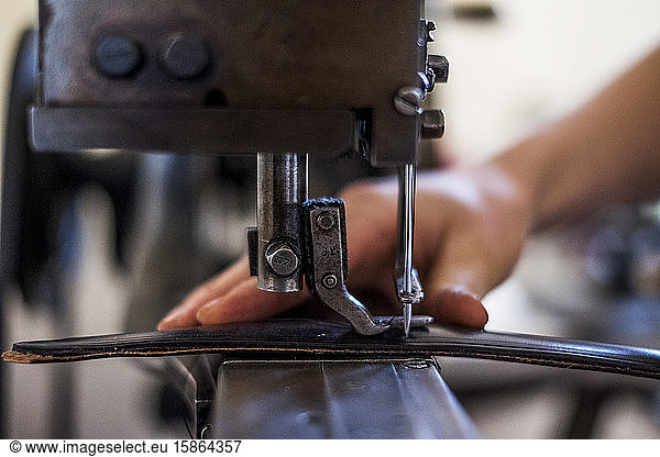 Close up of person sewing piece of leather to make a saddle.