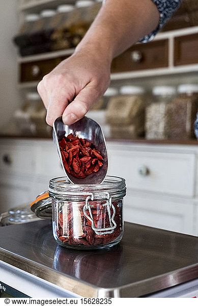 Close up of person weighing Goji berries in glass jar on kitchen scales.