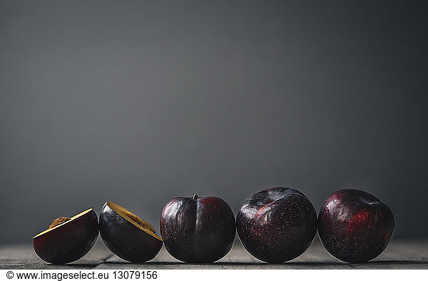 Close-up of plums arranged on wooden table against gray background