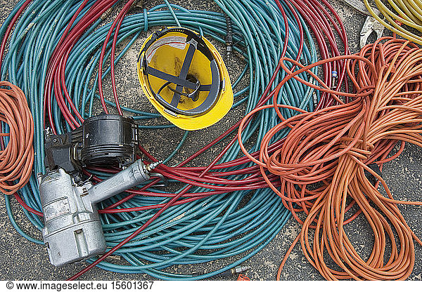 Close-up of power cords and air hoses with a nail gun and a hardhat at a construction site
