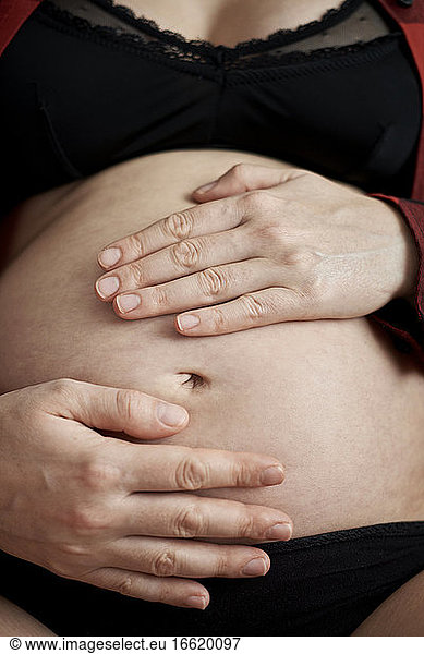 Close-up of pregnant woman with hands on stomach sitting at home