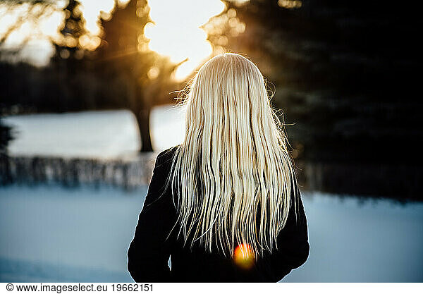 Close up of rear view of teen girl with long blond hair standing