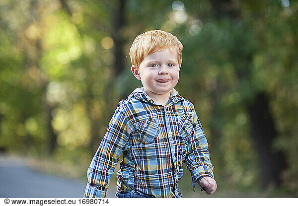 Close up of red haired toddler boy walking with tongue out outside