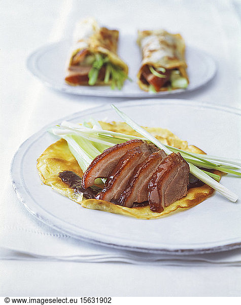 Close-up of roasted goose breast with pancakes and scallions served in plates on table