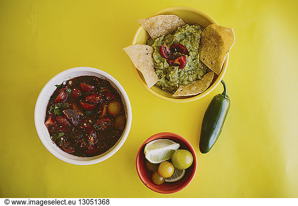 Close-up of salsa and guacamole served with ingredients on yellow background