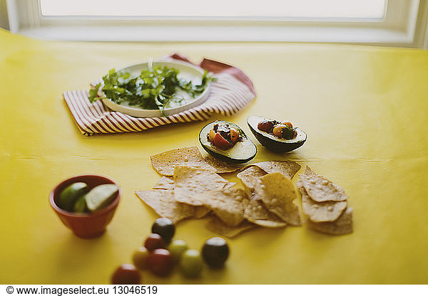 Close-up of salsa served in avocados with nacho chips on yellow table