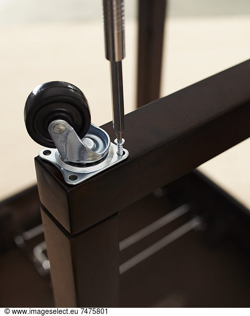 Close-up of Screwdriver Attaching Caster Wheel to Table