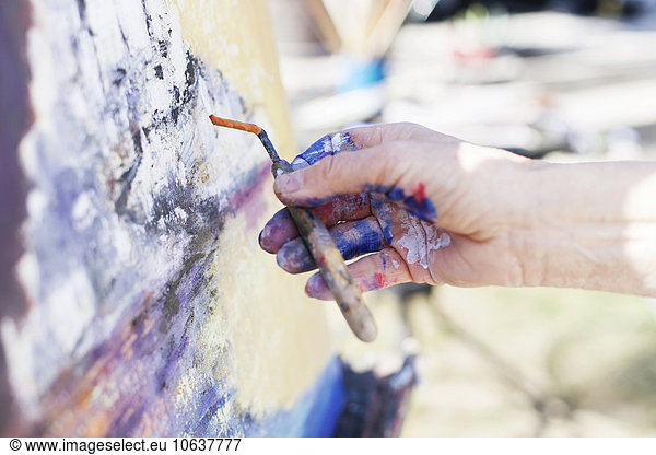 Close-up of senior female artist using painting knife on canvas outdoors