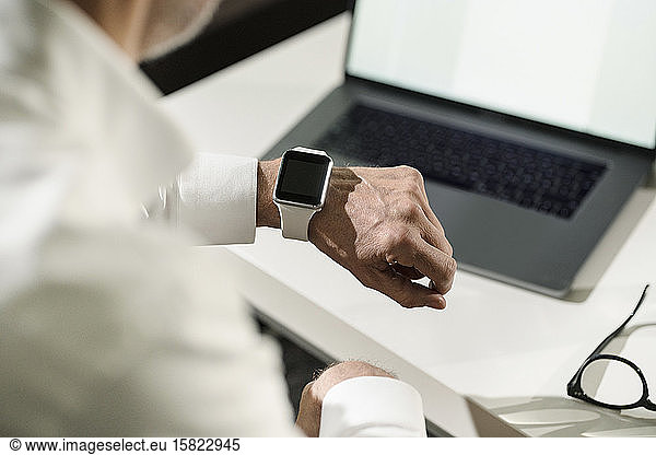 Close-up of senior man's hand with smartwatch and laptop